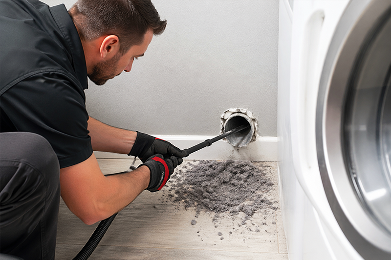 Dryer vent cleaning service removing lint buildup from wall duct in laundry room